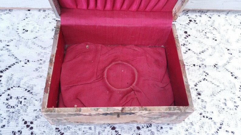 May include: An antique wooden box with a red velvet lining and a circular indentation in the center. The box is painted with a marbled pattern.