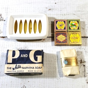 May include: A collection of vintage soaps and a soap dish. The soaps include a bar of "P and G The White Naphtha Soap" and several boxed soaps with labels like "Lavande" and "Rose The". A white rectangular soap dish with oval cutouts is also present.