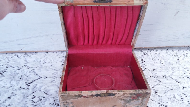 May include: An antique wooden box with a red velvet interior. The box has a hinged lid and a small ring holder inside.