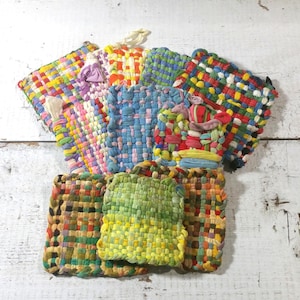May include: A collection of colorful, woven potholders in various sizes and patterns. The potholders feature a mix of bright colors, including red, blue, yellow, and green. Each potholder has a loop for hanging.