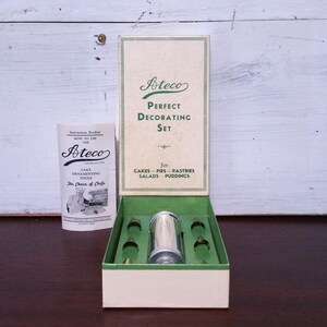 Puede incluir: Un juego de decoración de pasteles Ateco vintage en su caja original. El juego incluye una manga pastelera plateada y seis boquillas de metal. La caja es blanca con letras verdes y el texto "Ateco Perfect Decorating Set for Cakes - Pies - Pastries Salads - Puddings".