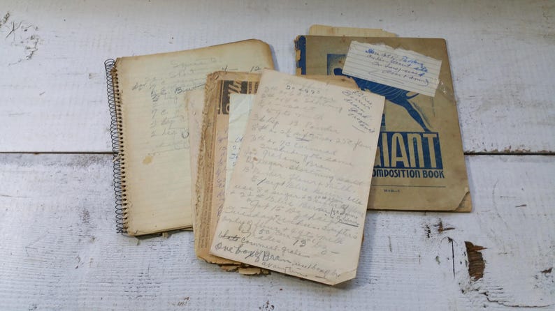 May include: A collection of vintage paper items, including a spiral-bound notebook and several loose sheets of handwritten notes. A composition book with the word "GIANT" is also present. The items are aged with a sepia tone.