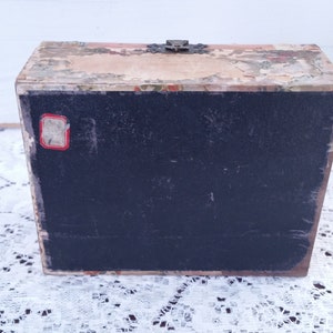 May include: A vintage wooden box with a black interior and a floral design on the top and bottom. The box has a metal latch and a small red label on the front.