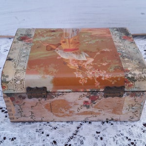 May include: A vintage wooden box with a floral design and a hinged lid. The lid features a colorful illustration of a woman holding a pitcher.