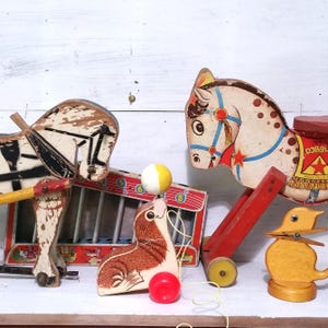 May include: A collection of vintage wooden toys, including a horse-drawn cart, a seal balancing a ball, a pull-along horse, and a wooden duck. The toys feature bright colors and show signs of wear, suggesting they are well-loved.