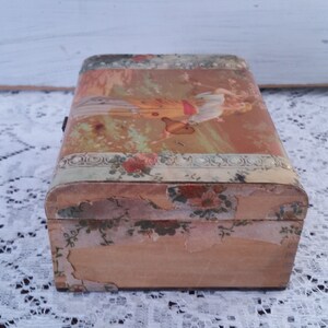 May include: A vintage wooden box with a floral design and a faded image of a woman on the lid. The box is in a worn condition, with some of the paper peeling off.