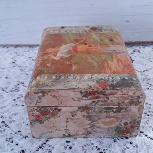 May include: A vintage wooden box with a floral design and a faded image of a woman on the lid. The box is painted in shades of pink, green, and brown.