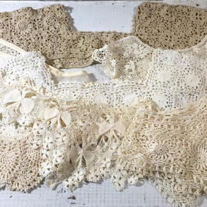May include: Assortment of vintage crochet lace pieces in various off-white and beige tones. The collection includes collars, doilies, and decorative elements with floral and geometric patterns. The delicate handmade textiles are arranged on a white surface.
