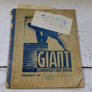 May include: A vintage "Giant Composition Book" with a blue and tan cover. The cover features a blue graphic of a person and the words "GIANT COMPOSITION BOOK". A handwritten note is attached to the cover.
