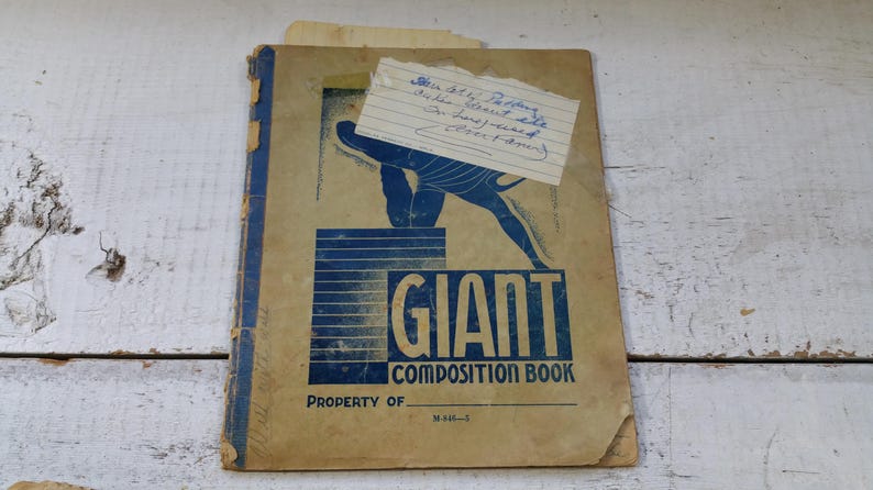 May include: A vintage "Giant Composition Book" with a blue and tan cover. The cover features a blue graphic of a person and the words "GIANT COMPOSITION BOOK". A handwritten note is attached to the cover.