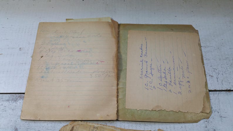 May include: An open vintage recipe book with handwritten recipes on aged paper. The left page has a list of ingredients and instructions, while the right page features a different recipe. The book is open, revealing the contents.