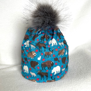 May include: A blue winter hat with a furry pom pom. The hat is covered in a pattern of various animals, including bears, moose, and foxes.