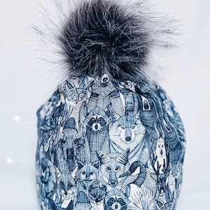 May include: A blue and white winter hat with a black and white animal print. The hat has a fluffy black pom-pom on top.