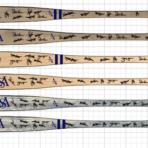 May include: Six wooden baseball bats with blue and white stripes and the letters "USA" painted on the handle. Each bat is covered in black ink signatures.