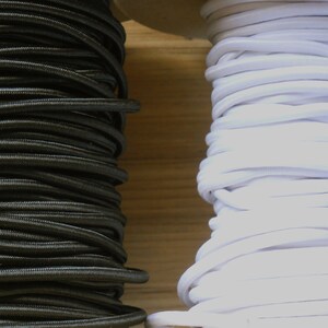 May include: Two spools of elastic cord, one black and one white. The spools are side-by-side on a wooden surface.