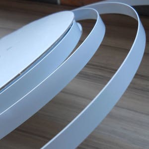 May include: Close-up of white edge banding for furniture, showing the smooth, rounded edges and light blue colour.