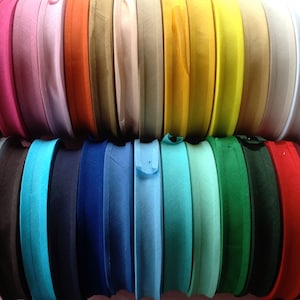 May include: A collection of colourful fabric trim rolls in various colours, including pink, orange, beige, yellow, green, blue, and red. The trim is arranged in two rows, with the top row showing the lighter colours and the bottom row showing the darker colours.