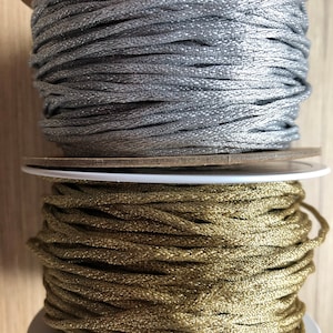 May include: Two spools of metallic thread, one silver and one gold. The spools are stacked on top of each other.