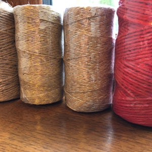 May include: Four spools of twine, one brown, one gold, one silver, and one red. The spools are wrapped in clear plastic.