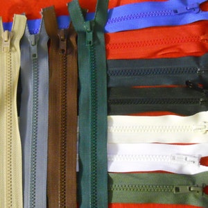 May include: Assortment of zipper closures in various colours, including beige, grey, brown, green, red, blue, black, and white. The zippers are arranged in rows and are all closed.