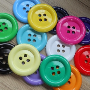 May include: Assortment of colourful plastic buttons with four holes each. The buttons are in various colours, including yellow, pink, green, blue, white and black.