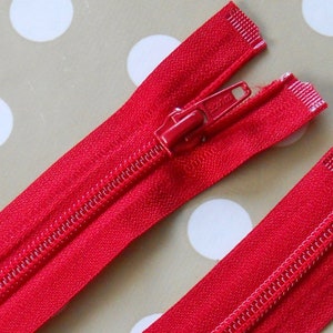 May include: Two red zips with silver pulls. The zip on the left is open and the zip on the right is closed.
