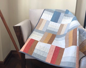 Può includere: Una trapunta patchwork con un motivo geometrico in tonalità di blu, marrone, beige e rosa. La trapunta è realizzata in tessuto di lino e ha un design semplice e moderno.