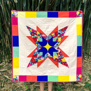 May include: A colorful quilt with a large star design in the center. The star is made of various floral fabrics in shades of red, pink, blue, and yellow. The quilt is bordered with strips of fabric in shades of red, orange, yellow, green, and blue.