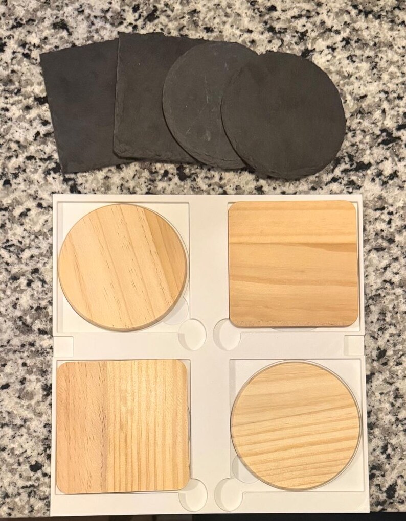 May include: A set of coasters in various shapes and materials. There are four wooden coasters in a white tray, two square and two round. Above them are three round and two square slate coasters. The coasters are designed to protect surfaces from heat and moisture.