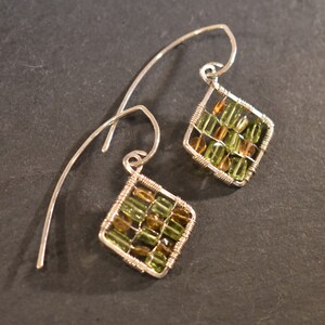 May include: A pair of silver earrings featuring green and brown gemstone accents. The gemstones are set in a wire cage design, creating a geometric pattern.