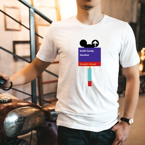 Op de afbeelding: Wit T-shirt met een paars en blauw bord met de tekst "Smith Family Vacation Straight Ahead" met een Mickey Mouse-hoofd en een pijl die omhoog wijst.
