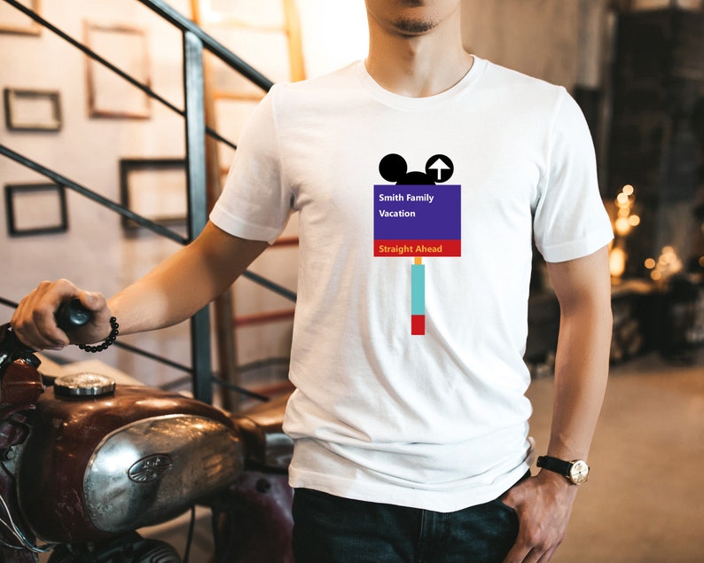 Op de afbeelding: Wit T-shirt met een paars en blauw bord met de tekst "Smith Family Vacation Straight Ahead" met een Mickey Mouse-hoofd en een pijl die omhoog wijst.
