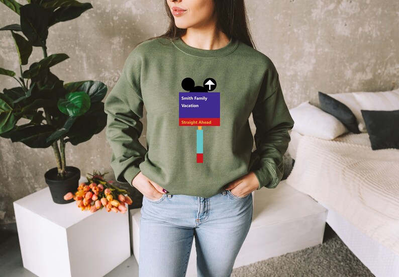 Op de afbeelding: Een groen sweatshirt met een afbeelding van een Mickey Mouse-hoofd en een bord met de tekst "Smith Family Vacation Straight Ahead".