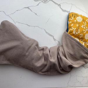 May include: A gray fabric heating pad with a yellow floral print cover. The heating pad is folded in half and the cover is partially pulled back to reveal the floral print.