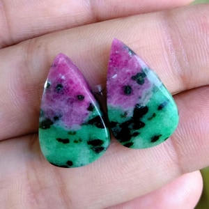 Może przedstawiać: Dwa zielone, różowe i czarne kamienie szlachetne w kształcie łzy. Kamienie szlachetne są wypolerowane i mają gładkie, błyszczące wykończenie.