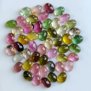 May include: A collection of numerous oval-shaped, faceted tourmaline gemstones in a variety of colors including shades of pink, green, yellow, and brown. The stones are arranged in a loose cluster, each displaying a polished, reflective surface.