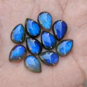 May include: A collection of ten teardrop-shaped labradorite gemstones. The stones display a vibrant blue iridescence with hints of green and gray. Each polished stone has a smooth, glossy surface, perfect for jewelry making or collecting.