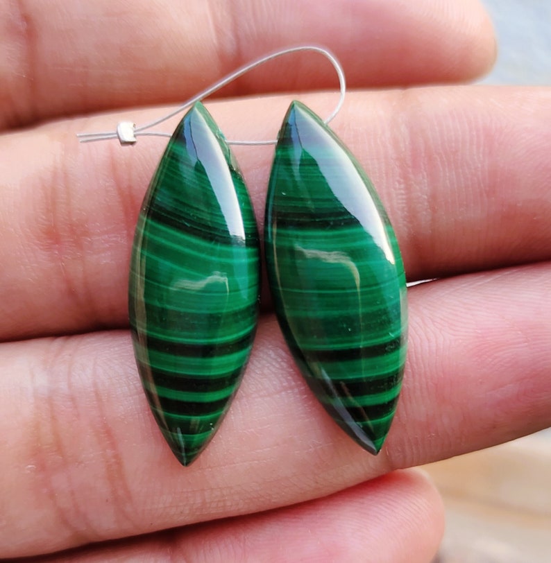 May include: A pair of green malachite gemstone earrings in a marquise shape. The earrings are a deep green color with dark green veins.