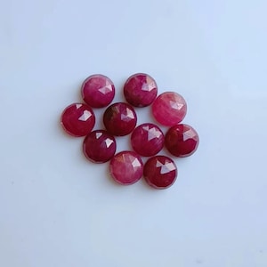 Könnte beinhalten: Eine Ansammlung von zehn runden, facettierten Edelsteinen in verschiedenen Schattierungen von Dunkelrosa und Rot. Jeder Stein weist eine geometrische, mehrfach facettierte Oberfläche auf, die das Licht reflektiert und ein Funkeln erzeugt.