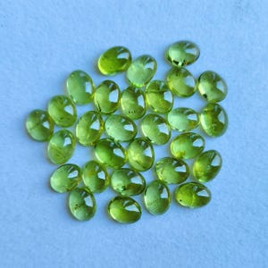May include: A collection of 20 green oval-shaped gemstones. The stones are smooth and polished, with a slight shimmer.
