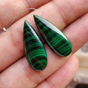 May include: A pair of green malachite teardrop-shaped gemstone pendants with a silver wire loop for hanging.