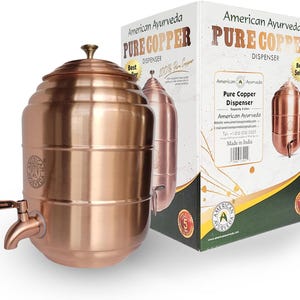 May include: A cylindrical copper water dispenser with a matching lid and a spigot, featuring the American Ayurveda logo. It is displayed next to its white cardboard packaging box, which displays the text Pure Copper Dispenser and 5 Liter capacity.