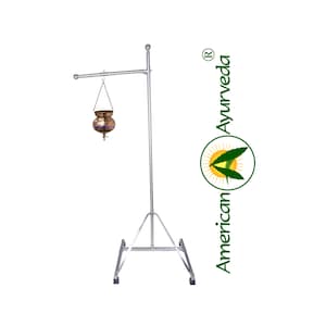 May include: A silver metal stand with a tripod base and a horizontal arm. A copper pot hangs from the arm. The stand is labeled "American Ayurveda" with a green leaf logo.