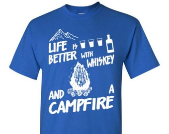 May include: A royal blue t-shirt with white text that reads "Life is better with whiskey and a campfire". The text is surrounded by a mountain, three glasses of whiskey, and a bottle of whiskey.
