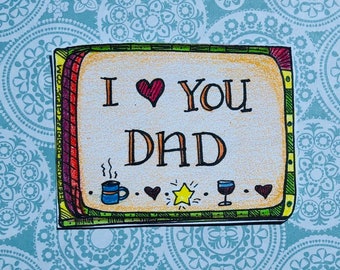 May include: A colorful card with a red heart and the text "I love you Dad" in a decorative frame. The card has a coffee cup, a star, a wine glass, and hearts.