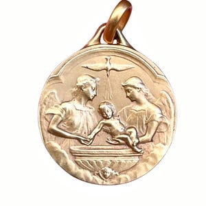 May include: A round gold pendant featuring a relief design of two winged figures standing on either side of a basin, holding a small child. Above the child, a dove is depicted in flight. The pendant includes a gold bail at the top for suspension.