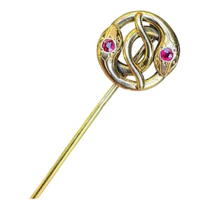 Peut inclure: Une épingle à cravate en or présentant un motif circulaire formé par deux serpents entrelacés. Chaque tête de serpent est ornée d'une petite pierre précieuse rose vif et ronde en guise d'œil. Le métal a une finition polie et une tige.