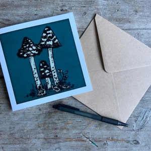 May include: A teal blue card with a white border features a black and white illustration of three mushrooms. The mushrooms have a striped pattern and are set against a teal blue background.