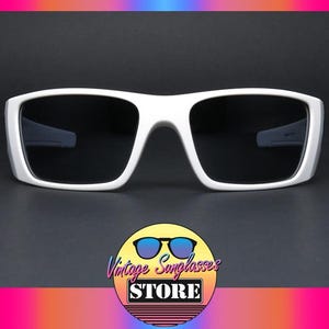 May include: White sunglasses with a thick frame and dark lenses. The sunglasses have a rectangular shape and a modern design. The image also includes a logo for "Vintage Sunglasses STORE".