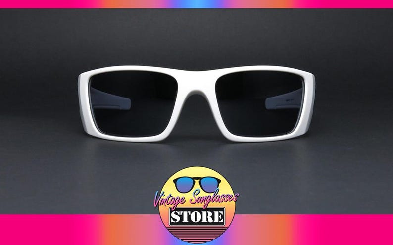 May include: White sunglasses with a thick frame and dark lenses. The sunglasses have a rectangular shape and a modern design. The image also includes a logo for "Vintage Sunglasses STORE".